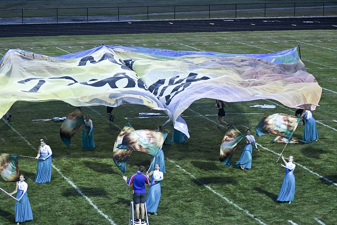 The giant flag that reads ÒMy DestinyÓ flies over the Jay County High School Marching PatriotsÕ color guard members Tuesday night during the bandÕs Indiana State Fair preview performance. JCHS will take the track for competition at the state fair at 2:09 p.m. Friday. Preliminary awards are at 4:30 p.m., with the top 16 returning for finals at 8 p.m. (The Commercial Review/Ray Cooney)