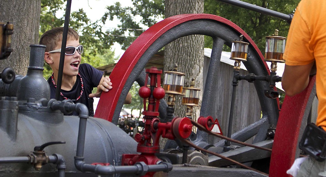 Lane Holtzleiter, 12, helps his father Steve turn the wheel on a Spang and Company engine from Butler, Pennsylvania, on Wednesday during the Tri-State Antique Engine and Tractor Show at Jay County Fairgrounds. The show continues today through Saturday. (The Commercial Review/Bailey Cline)
