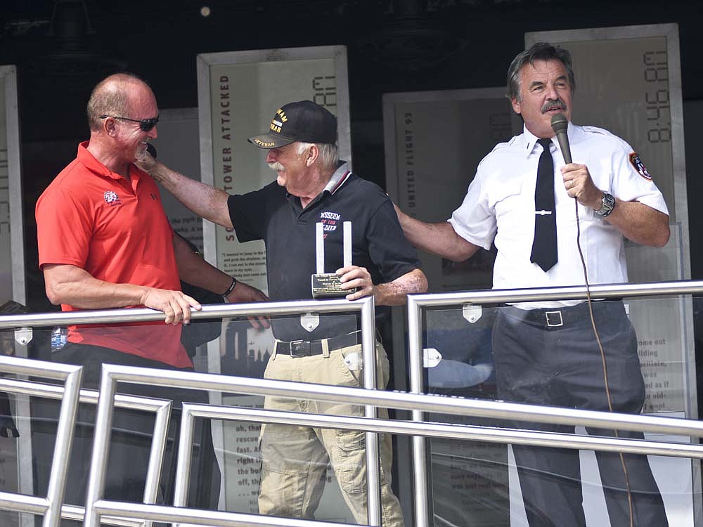 Billy Puckett (left) and Pat Clancy (right) of the Tunnel to Towers Foundation present Jim Waechter of Portland's Museum of the Solider with steel from the World Trade Center during a closing ceremony Sunday for the 9/11 NEVER FORGET Mobile Exhibit at Jay County Fairgrounds. The exhibit was on display in Jay County on Friday, Saturday and Sunday. The steel from the World Trade Center will be displayed at Museum of the Soldier. (The Commercial Review/Ray Cooney)