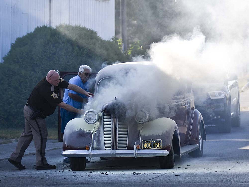 Smoke pours from a vehicle stopped facing north on Ship Street at its intersection with Water Street while Patrick Wells of Jay County Sheriff's Office attempts to extinguish the fire. Portland Fire Department arrived and put out the fire, with Portland Police Department also assisting at the scene. (The Commercial Review/Ray Cooney)