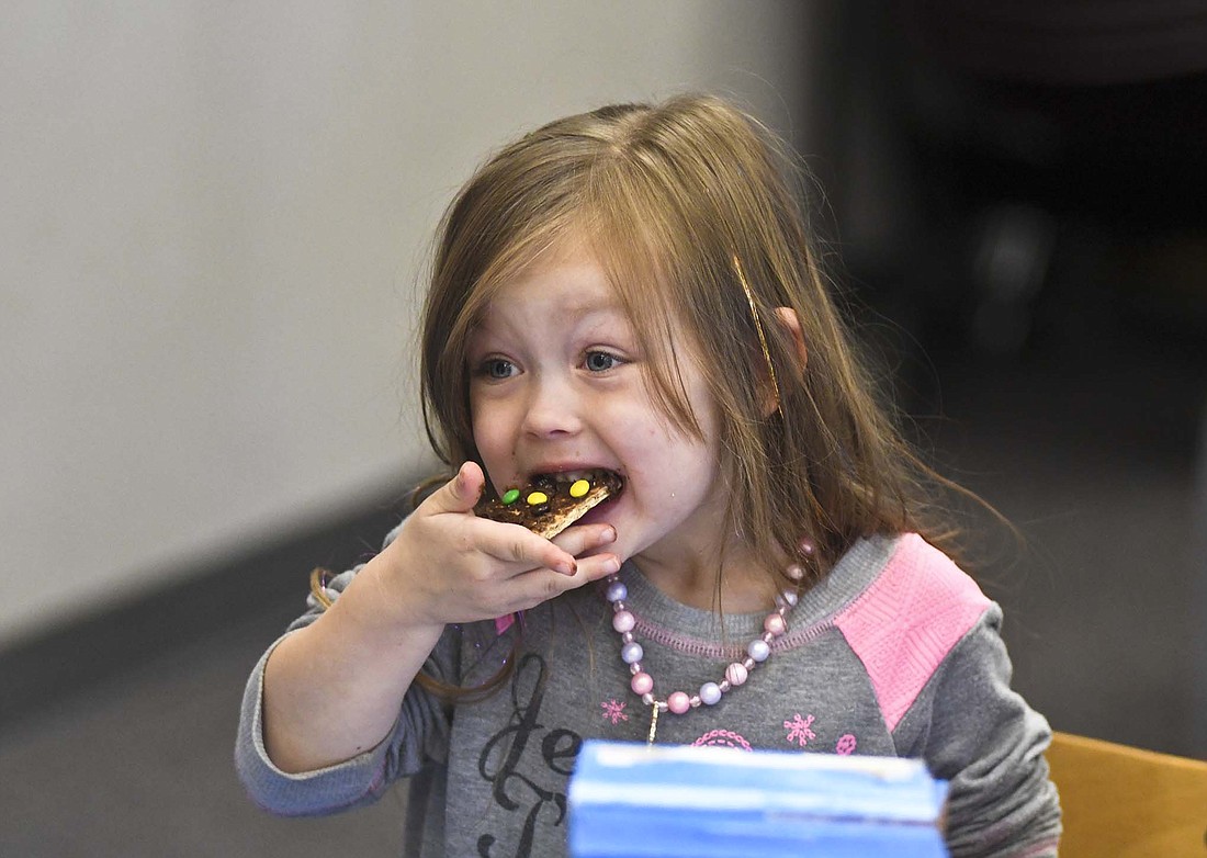 Wynnie Hardwick, 3, takes a bite of a snack of graham cracker, M&Ms and chocolate frosting during story time Tuesday morning at Jay County Public Library in Portland. Children sang songs, listened to stories about music and then visited stations that offered toys, crafts, games, finger painting and snacks. The next family story time at the library is scheduled for 10 a.m. Oct. 24. It is also holding a Fall into Fun event from 5 to 7 p.m. Thursday with activities including an indoor maze, games, popcorn, apple cider pumpkin picking and wagon rides. (The Commercial Review/Ray Cooney)