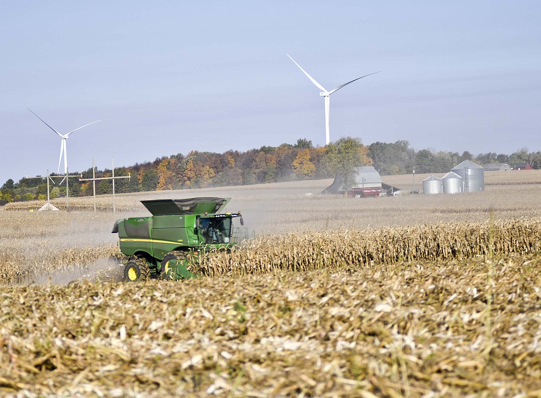 A farmer harvests corn in a combine Tuesday morning in front of a couple of wind turbines that are part of Bitter Ridge Wind Farm in a field on the north side of county road 650 South, just east of county road 550 West. The weather was good for harvesting Tuesday with sunny skies and the high climbing to near 80 degrees. (The Commercial Review/Ray Cooney)