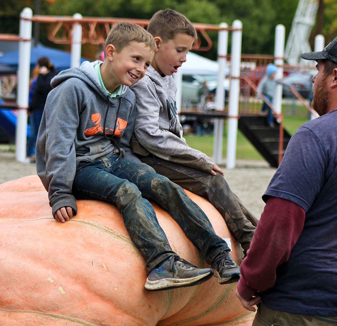 Maverick and Wyatt Hodge chat with their father, Mikkal Hodge, while sitting on their award-winning giant pumpkin Saturday. The Madison County family won the adult class in this year’s Pennville Pumpkin Festival with their pumpkin coming in at 1,778 pounds. (The Commercial Review/Bailey Cline)