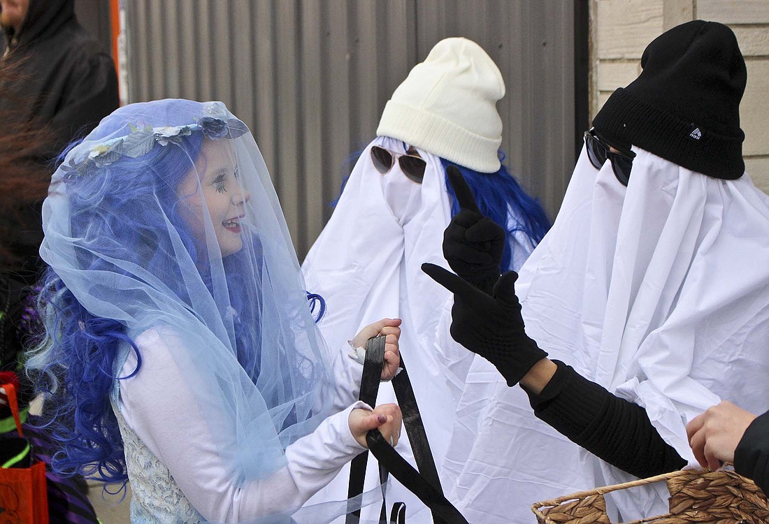 Eight-year-old Raylee Laxton, above, talks to a ghost (Alivia Rowles) during the Jay County Chamber of Commerce Merchants Trick or Treat on Tuesday. Rowles and her fellow Beauty Bar coworkers were set up outside the business’ new location along Meridian Street. Below, 5-year-old Emerson Bost digs through a tub of candy while trick-or-treating along Meridian Street.