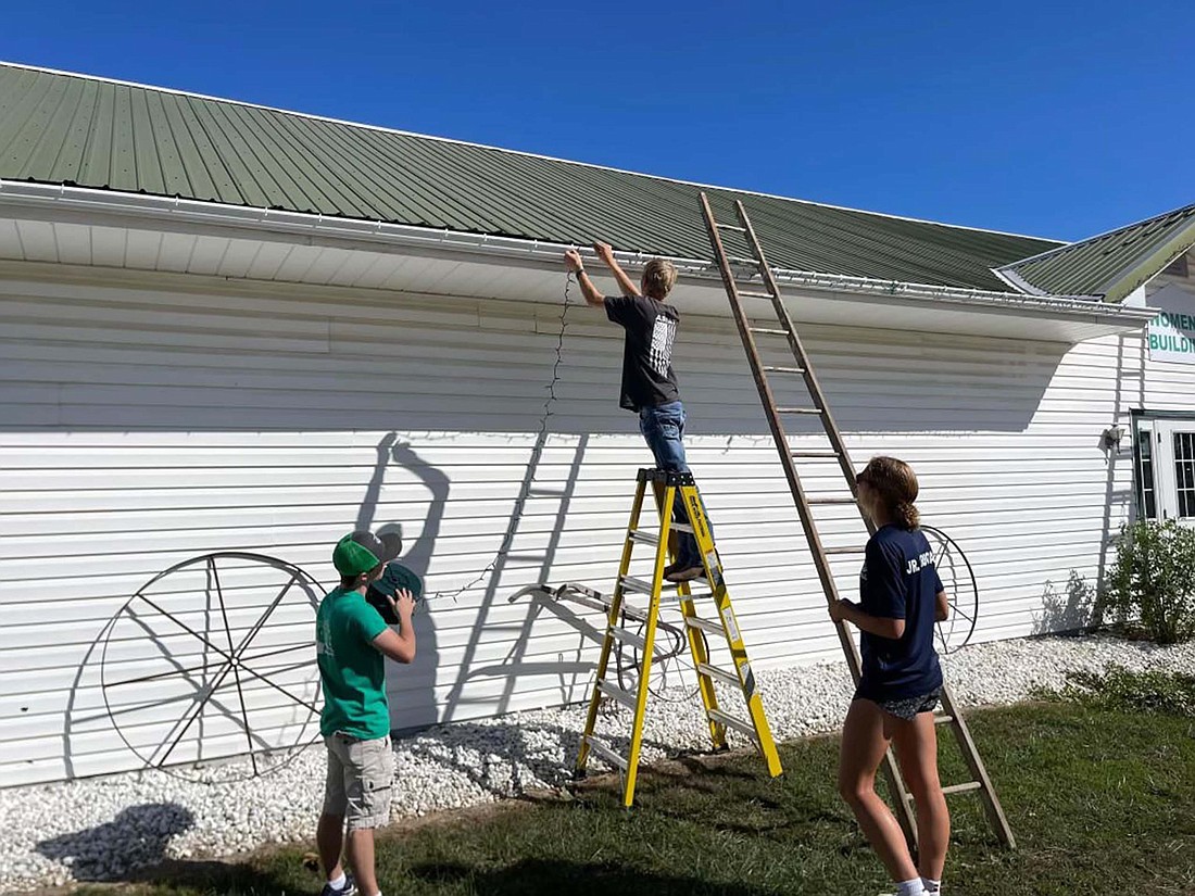 Cruis’n the HoliJay Lights at the Fairgrounds is adding a new feature this year with the Mistletoe Market on Dec. 2. Pictured, fair board ambassadors, from left, Joey Hall, Mason Muhlenkamp and Molly Muhlenkamp hang lights in preparation for the event. Mistletoe Market will feature 25 booths of Christmas decorations, crafts, candy and other gift options for the holiday season. (Photo provided)