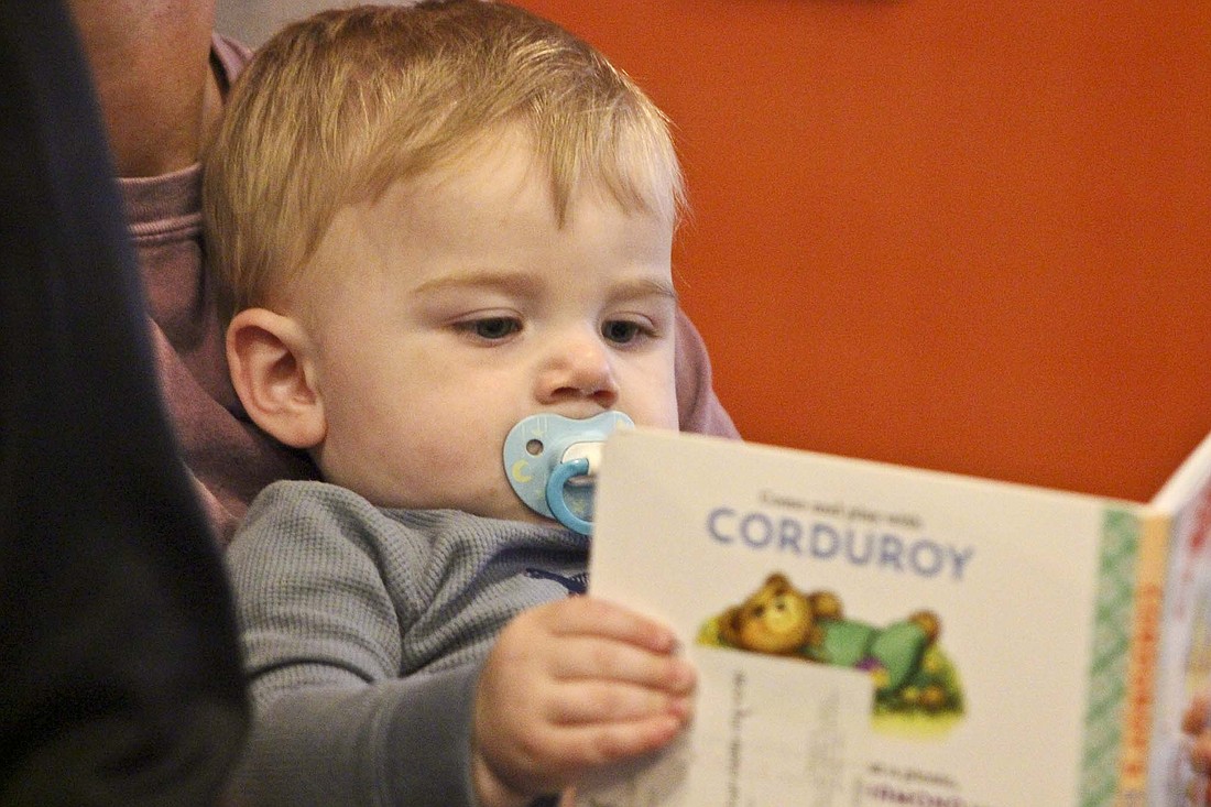 One-year-old Knox Willmann holds up a book while mother Ashley Willmann reads to him and his siblings in November at their home in rural Portland. The family is one of many families in Jay County benefitting from the Imagination Library program handled locally by Jay County REMC. (The Commercial Review/Bailey Cline)