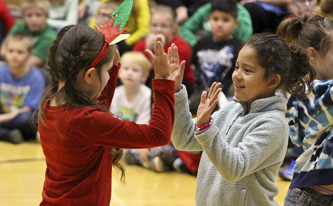 East Elementary second graders Addalyn Bost and Ashley Rodriguez dance together in front of the bleachers in East Jay Elementary’s gymnasium on Thursday during practice for their Christmas program. (The Commercial Review/Bailey Cline)