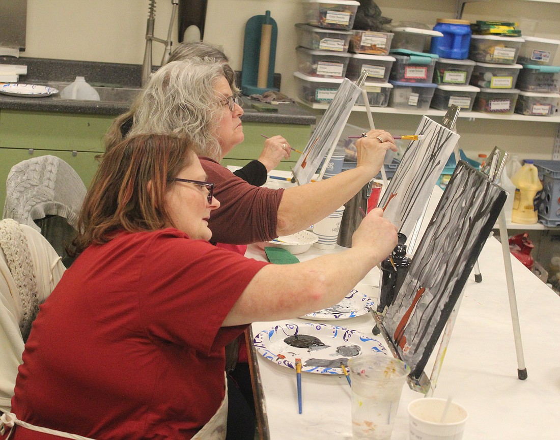 Kristine Alexander (foreground) and Pamela Straley paint Thursday evening during the Cookies and Canvas event at the Hudson Center for the Visual Arts on the Jay County Campus of Arts Place. About a dozen participants attended to paint a snowy forest scene featuring a fox. (The Commercial Review/Ray Cooney)