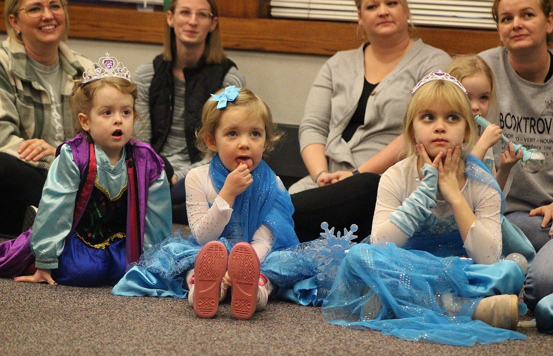 Cousins Charlotte Houck, 3, Kallie Carpenter, 3, and Victoria Glentzer, 7, watch as Anna and Elsa introduce themselves to the crowd Thursday at the start of the “Frozen” sing-along party at Jay County Public Library. (The Commercial Review/Bailey Cline)