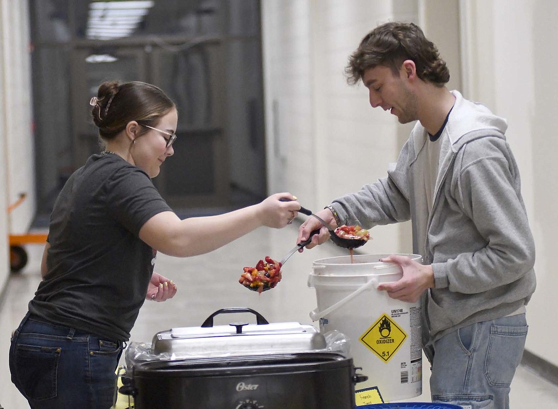 Jay County FFA members Ella Stockton and Nick Lyons scoop fruit salad out of a bucket in preparation for Thursday’s staff breakfast at Jay County Junior-Senior High School. The event was part of the chapter’s celebration of National FFA Week. (The Commercial Review/Ray Cooney)