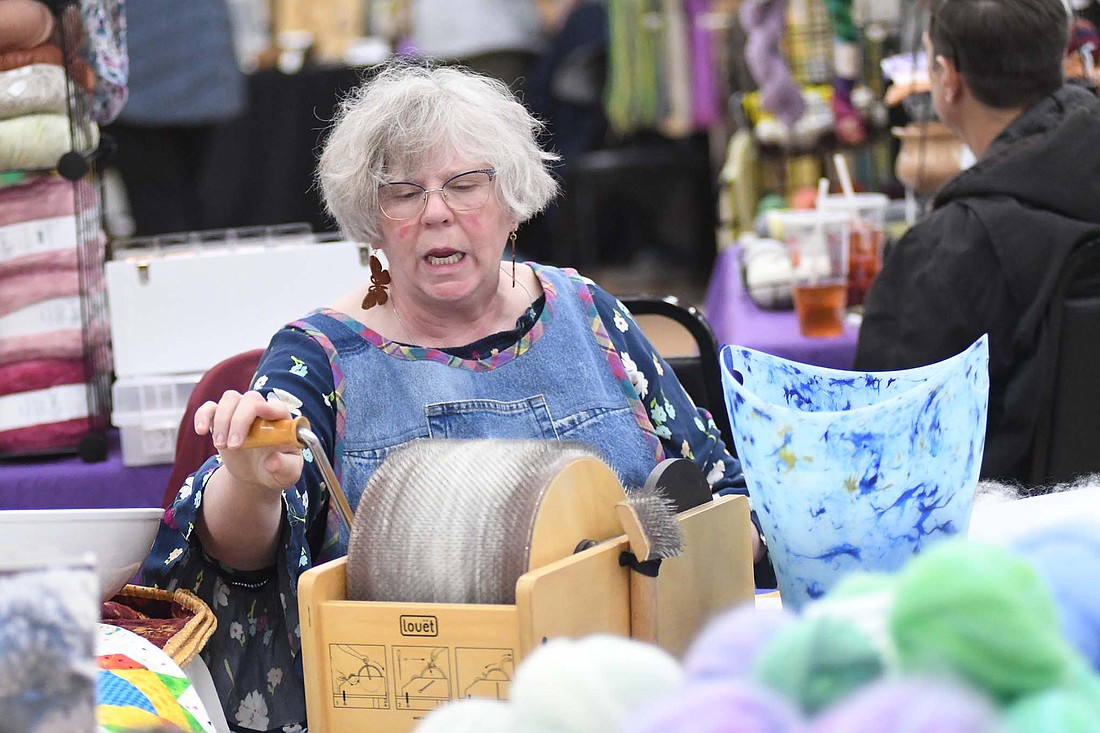 Nola Katinsky of Fort Wayne chats while working on spinning wool Friday during the Jay County Fiber Arts Festival hosted by Jay County Visitor and Tourism Bureau at Jay Community Center. Katinsky was at the event with Teasel Hill Angoras Farm. (The Commercial Review/Ray Cooney)