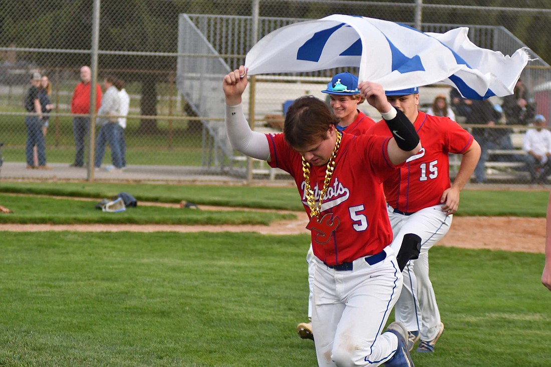 Parker Nichols, a senior at Jay County High School, carries the W flag as he leads the rest of the Jay County High baseball team to the center field flag pole after beating the Woodlan Warriors 2-1 on Thursday. Nichols drove in both runs for Jay County, including a walk off RBI single that prompted his teammates to put the JC chain on his neck. (The Commercial Review/Andrew Balko)