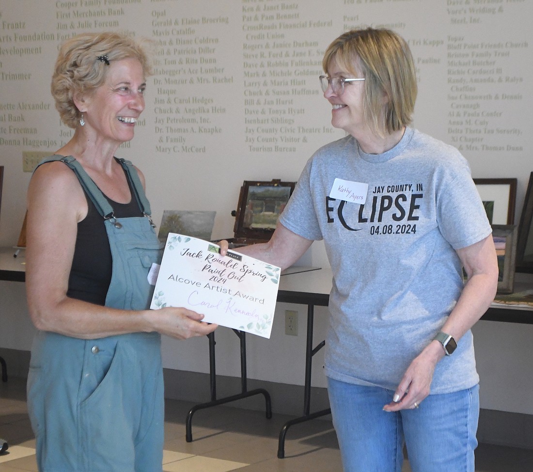 Carol Kennedy accepts the award from Alcove president Kathy Ayers during a ceremony Saturday evening at Arts Place to close the inaugural Jack Ronald Spring Paint Out. Kennedy’s winning piece for the ‘plein air’ event was a view of the Hood Building where Ronald worked for The Commercial Review for more than four decades. (The Commercial Review/Ray Cooney)