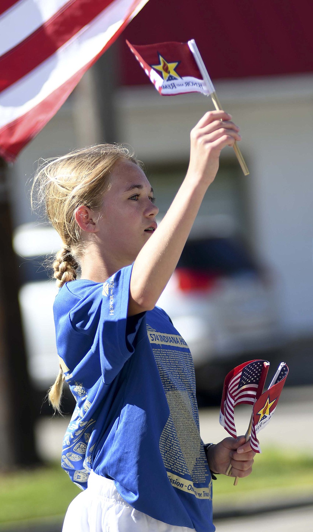 Addi Evitts holds up a small Honor and Remember flag Saturday morning at the Indiana Run for the Fallen stop in honor of Private Robert Leon McKinley, Specialist Justin Lee Mundy and Lance Cpl. Olivia L. Kustes. The run started its second day at Portland's Freedom Park and ended in Anderson. It was slated to finish with the Anderson to Indianapolis on Sunday. (The Commercial Review/Ray Cooney)