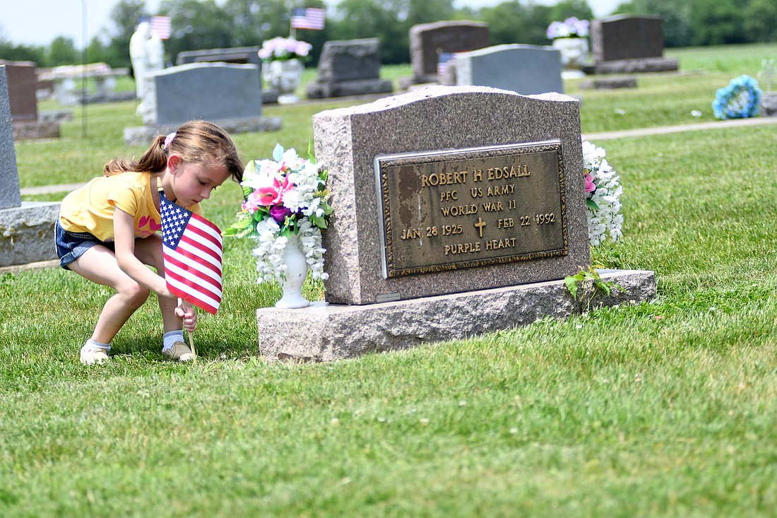 Seven-year-old Matilda Miller places a flag at the grave site of Robert H. Edsall — he served in the U.S. Army during World War II and was awarded a Purple Heart — on Friday afternoon at Center Cemetery in preparation for Memorial Day. Miller was part of a group of several Jay County Girl Scout troops placing flags at the cemetery on county road 500 West, just north of Indiana 26. Memorial Day services scheduled for this weekend include 2 p.m. Sunday at Gravel Hill Cemetery west of Bryant; 9 a.m. Monday at Claycomb Cemetery in Greene Township; 10 a.m. at the Redkey War Mother’s Memorial Monument; 11 a.m. Monday at Green Park Cemetery in Portland; and 11:15 a.m. at Hillcrest Cemetery south of Redkey. (The Commercial Review/Ray Cooney)