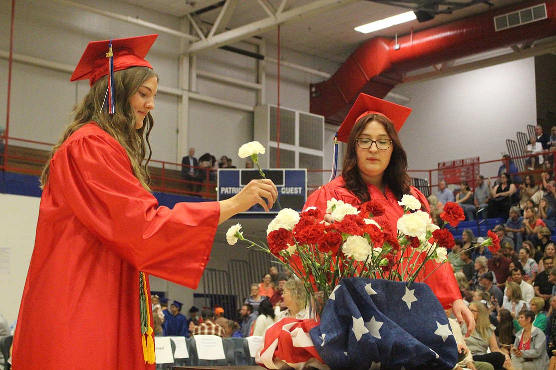 Breanna Dirksen and Ava Daniels place carnations in a vase Sunday during Jay County High School’s graduation ceremony. Students entered the gym for commencement with carnations in their hands, with each graduate placing a flower in a vase before walking to their seats. (The Commercial Review/Bailey Cline)