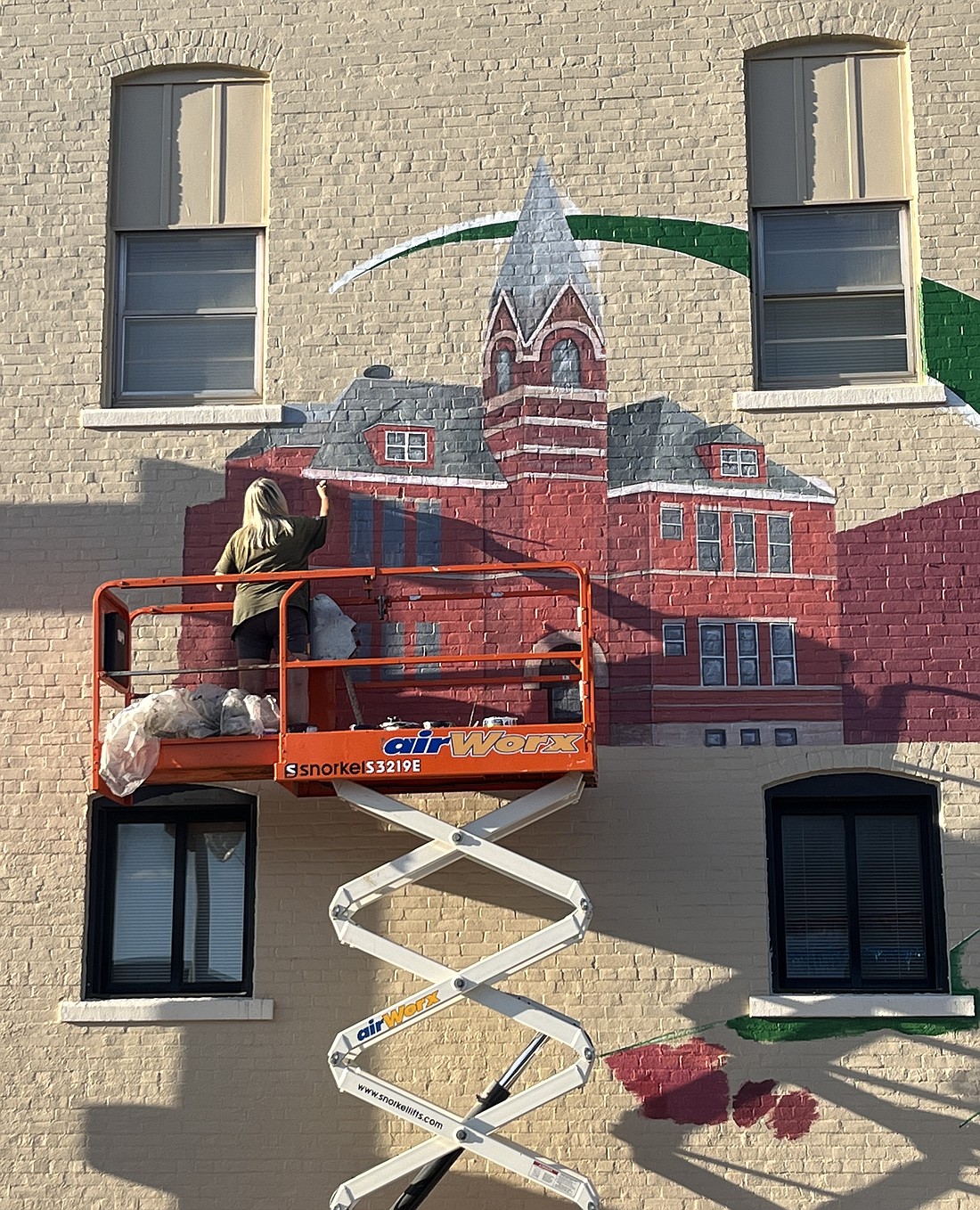 Artist Pam Bliss works on the new mural on the Commerce Street side of the Dunkirk City Building on Monday evening. The public art piece will feature two former Dunkirk high schools, the former Sutton School and the Dunkirk Speedcats logo. It is expected to be complete by the end of the week, weather permitting. (The Commercial Review/Ray Cooney)