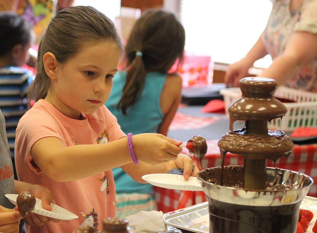 Penny Howell, 6, dips a strawberry in a chocolate fountain Thursday at Jay County Public Library during its Strawberry Fest. Families visiting the library had an opportunity to meet Indiana author Shannon Anderson, who wrote “I LOVE Strawberries!”, eat strawberry snacks and participate in strawberry themed games, crafts and activities. (The Commercial Review/Bailey Cline)