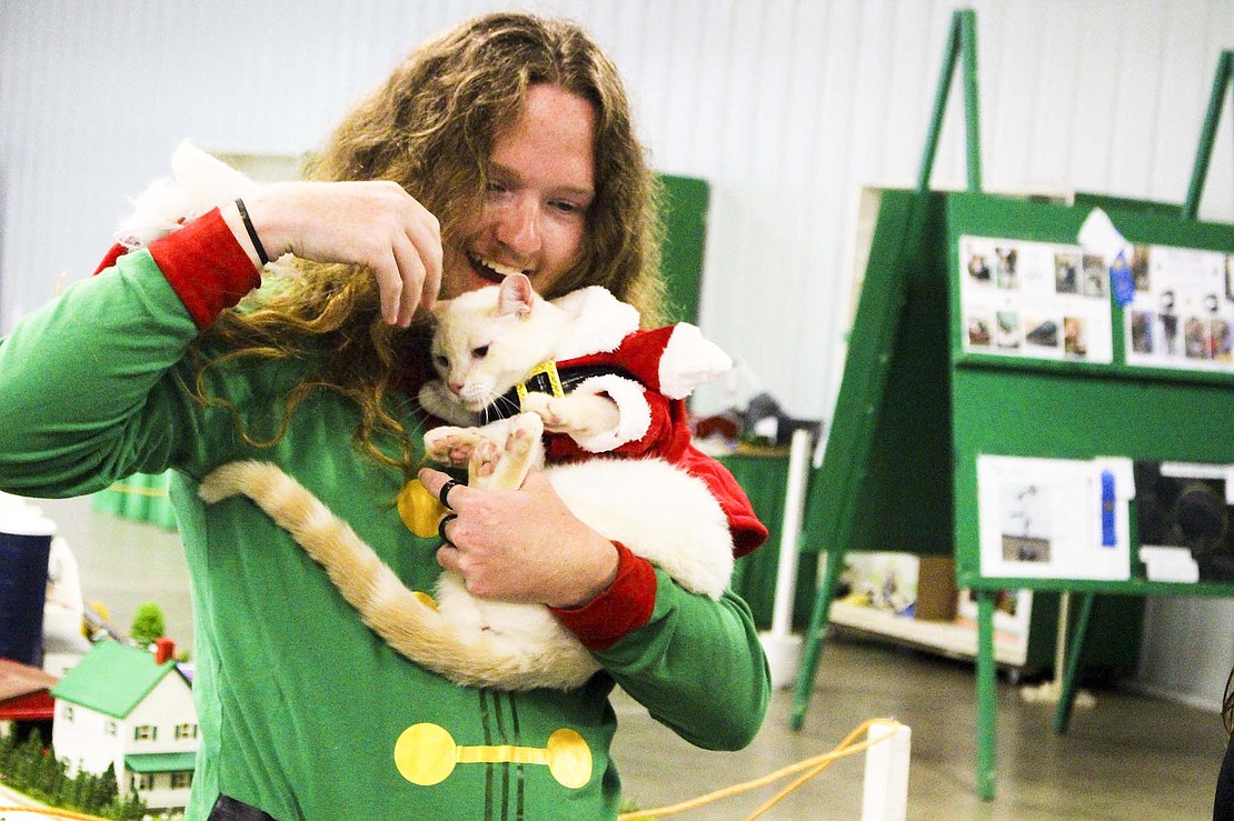 Dominic Steveson, 16, struggles as his cat, Zero, tries to wiggle out of his Santa Claus costume Monday during the cat show in the Bob Schmit Memorial Exhibition Hall. Steveson dressed as a Christmas elf to compliment Zero’s outfit for the costume contest portion of the cat show. (The Commercial Review/Bailey Cline)