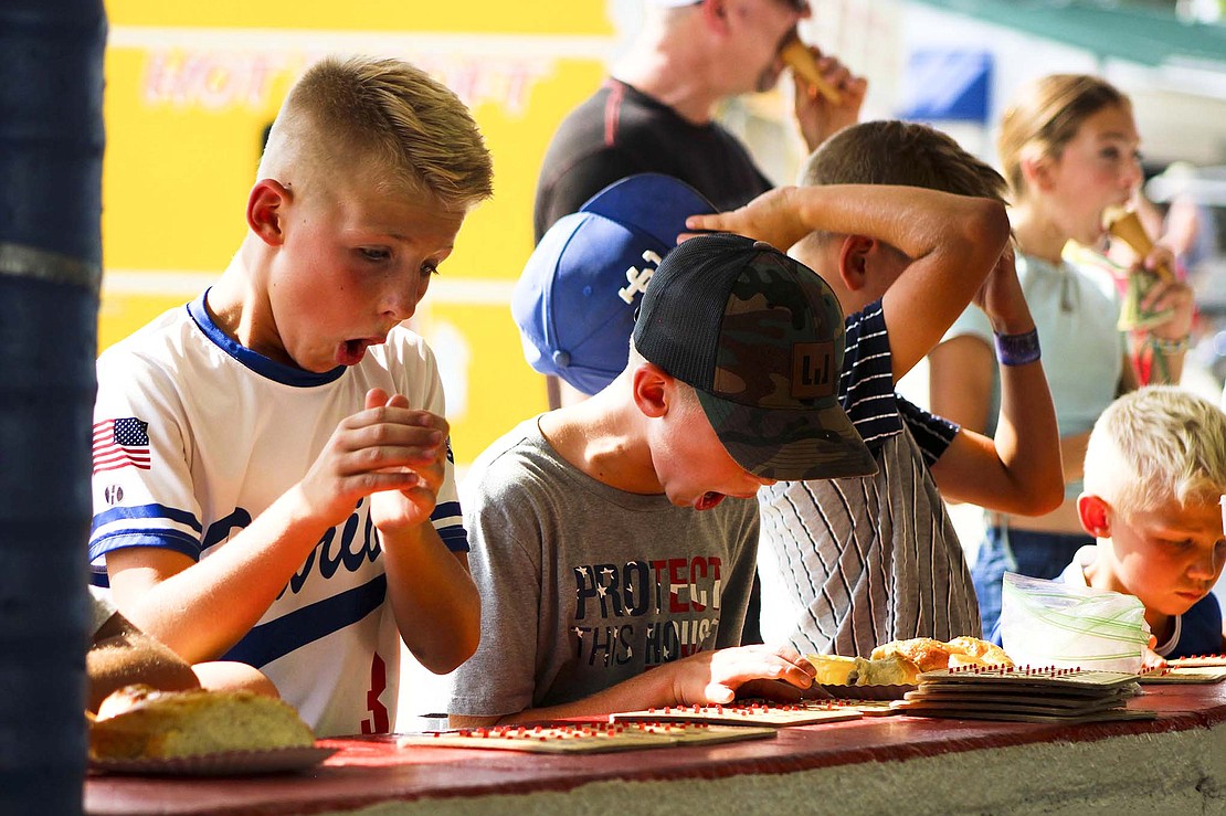 Easton Johnson, 11, Jackson Westgerdes, 10, and Dakota Johnson, 9, exclaim while filling out BINGO boards Monday afternoon. The American Legion Riders are hosting the BINGO stand this year. (The Commercial Review/Bailey Cline)