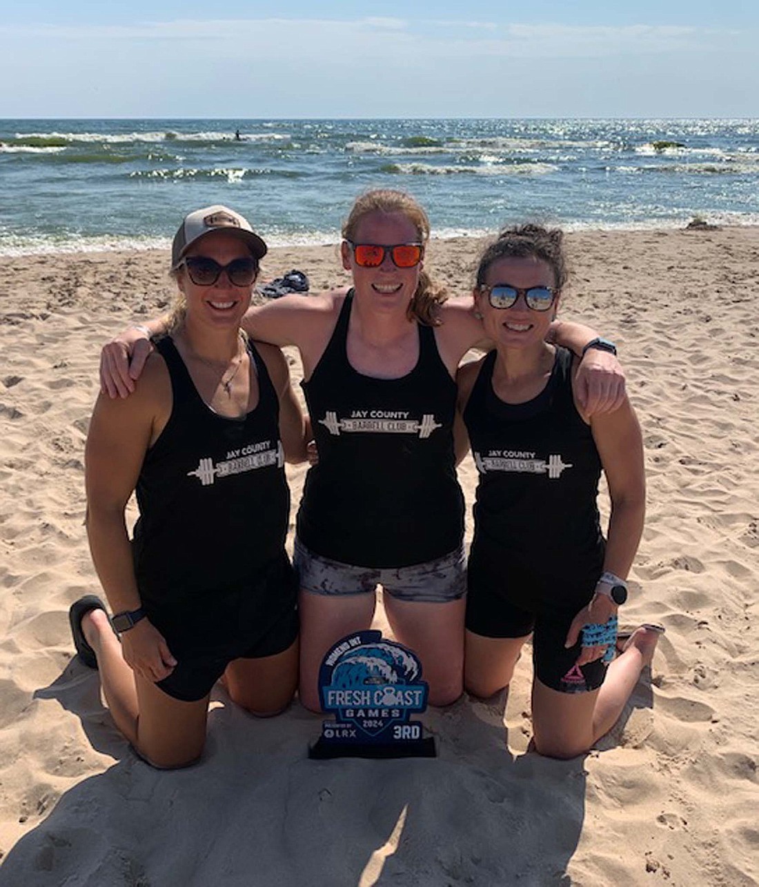 Pazia Williams, Carly Hess and Shawnda Roussey of the Jay County Barbell Club kneel on the beach with their third-place trophy from the Fresh Coast Fitness Games in Muskegon, Michigan. To take third, the trio had to compete in four workouts against 59 other teams from Indiana, Michigan, Alabama and Tennessee in the women’s intermediate division. (Photo provided)