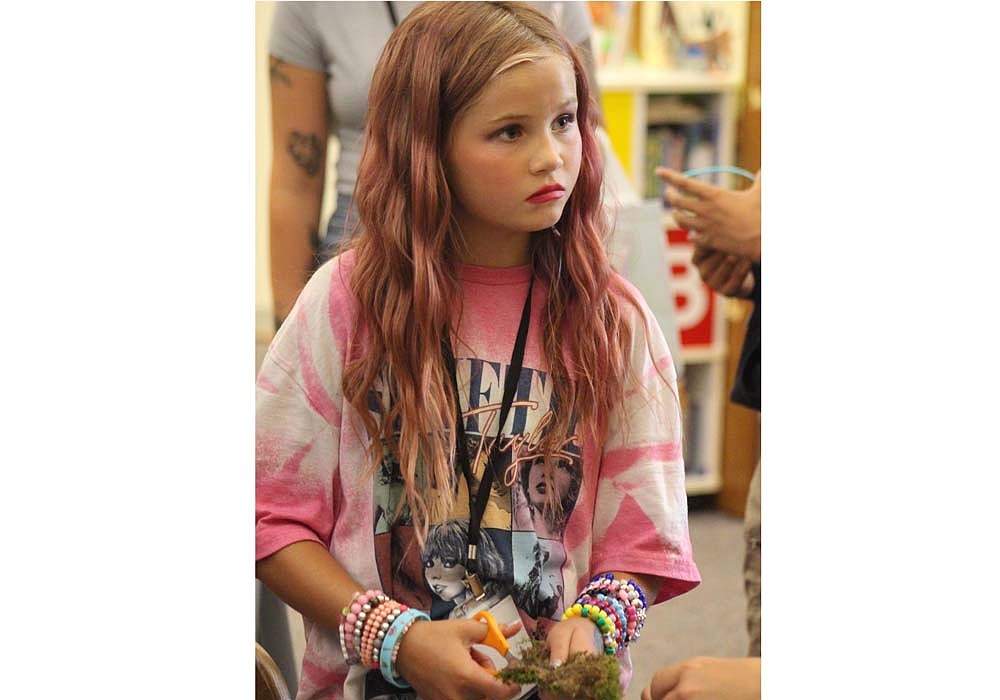 Elsie Gibbs (above), 10, looks up from cutting moss Tuesday during Jay County Public Library’s “A Night for the Swifties.” Gibbs and others decorated candles with moss at the station themed after Taylor Swift’s eighth album, Folklore. Additional stations themed after Swift and her albums were sprinkled across the library. Nine-year-old Clara Gossage (below) colors a paper guitar at another station. (The Commercial Review/Bailey Cline)