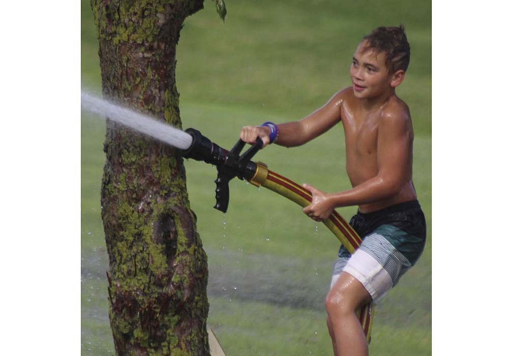 Kolton Anduiano, 10, aims a firehose at other children playing in the grass across from Ambassador Pool during Fort Recovery’s National Night Out event Sunday. Portland’s National Night Out is scheduled for Tuesday, Aug. 6, at Hudson Family Park. (The Commercial Review/Bailey Cline)