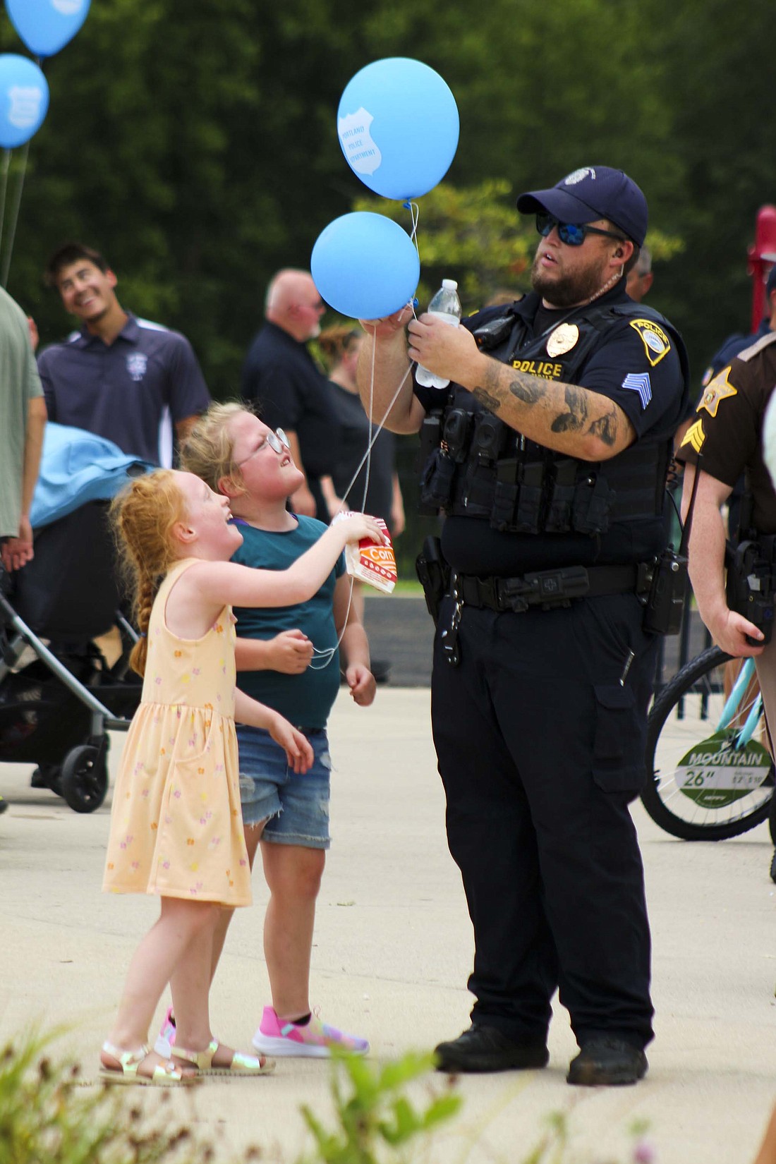 Twins Harper and Hadley McDavid, both 7, get help from father and Portland police officer Brandon McDavid with untangling their balloons Tuesday during Jay County’s National Night Out at Hudson Family Park. (The Commercial Review/Bailey Cline)