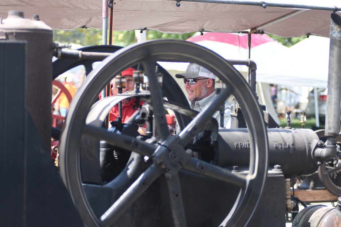 Visitors to the Tri-State Antique Engine and Tractor Show chat Saturday afternoon while an engine spins in front of them. The show concluded Saturday, and the 60th iteration of the annual event will be held next year. (The Commercial Review/Ray Cooney)