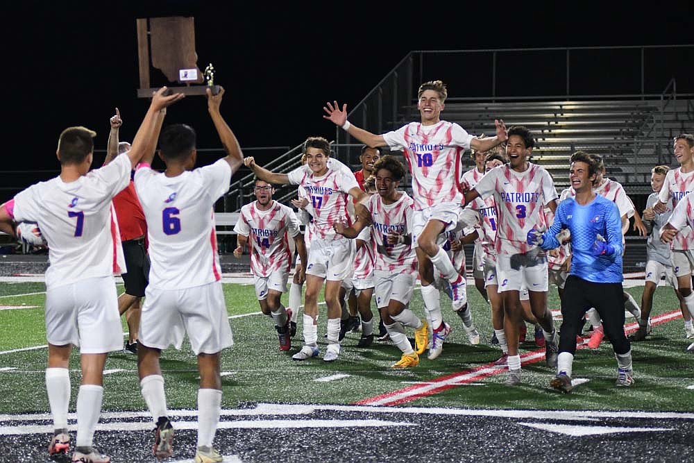 The Jay County boys soccer team charges to meet teammates Levi Muhlenkamp (7) and Dylan Marentes (6) after receiving the IHSAA Class 2A Sectional 23 trophy on Saturday. Marentes scored a key goal for the Patriots with just over two minutes remaining in regulation to force overtime. (The Commercial Review/Ray Cooney)