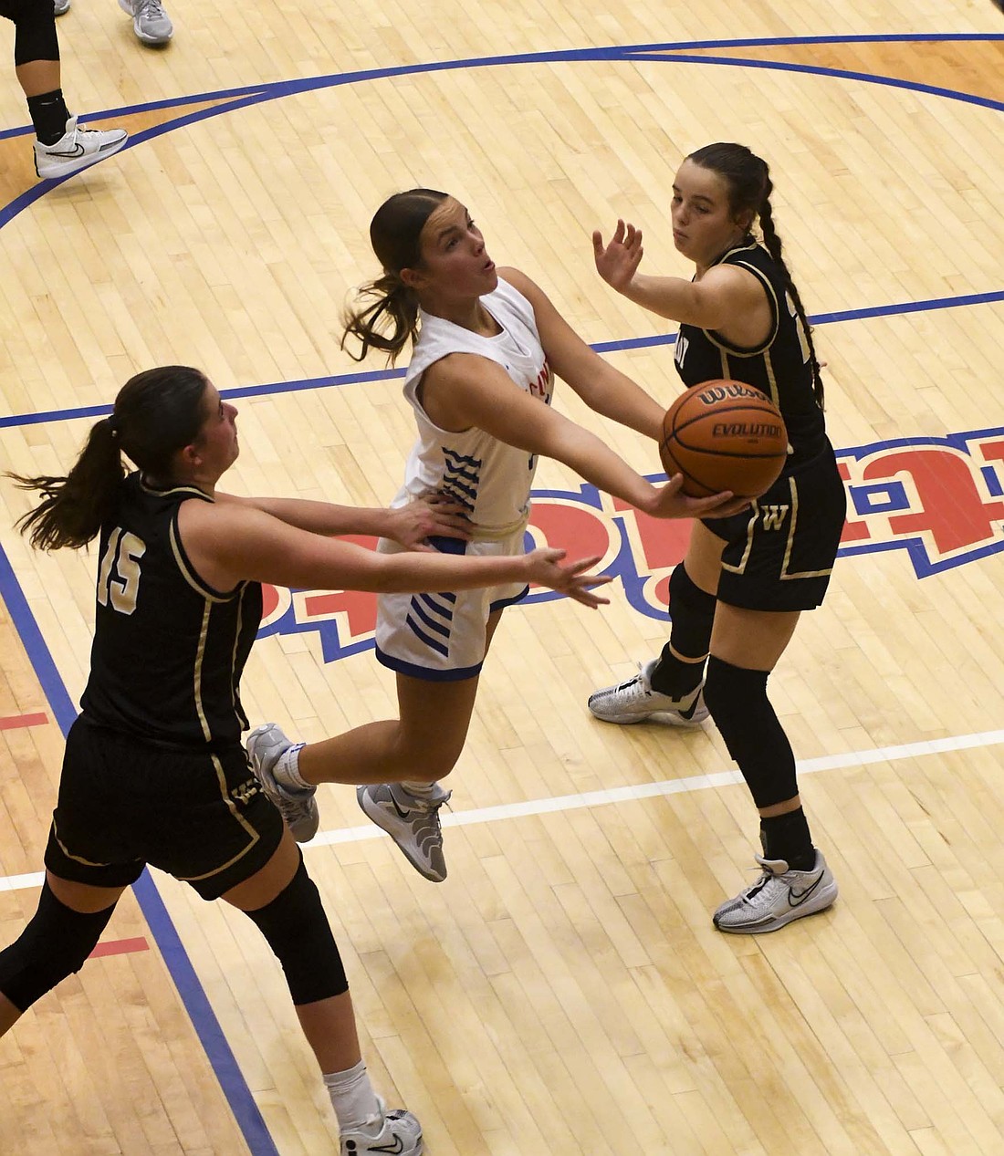 Jay County High School’s Elizabeth Brunswick glides in between Winchester’s Auden Hummel (15) and Kendall Patterson to take a finger roll in the second quarter on Saturday. Brunswick had a team-high seven rebounds, four assists and three blocks in the 42-30 victory. (The Commercial Review/Andrew Balko)