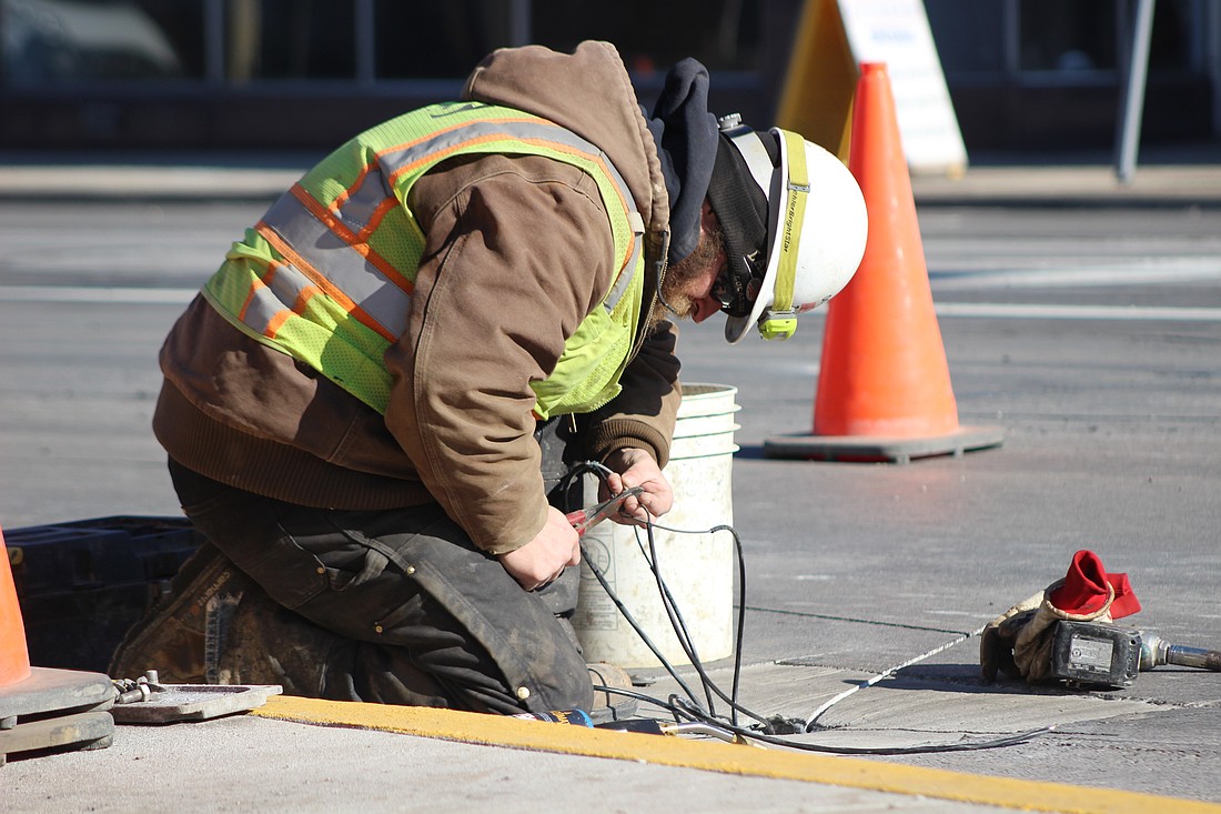 A Shambaugh & Son construction engineering worker adjusts wiring Thursday on Meridian Street (U.S. 27) next to its intersection with Main Street in Portland. Workers installed and adjusted wiring in the street and filled corresponding cuts made in the street Thursday. Some equipment for stop lights and pedestrian signals have recently reappeared along the road, which has had ongoing construction since last year. (The Commercial Review/Bailey Cline)