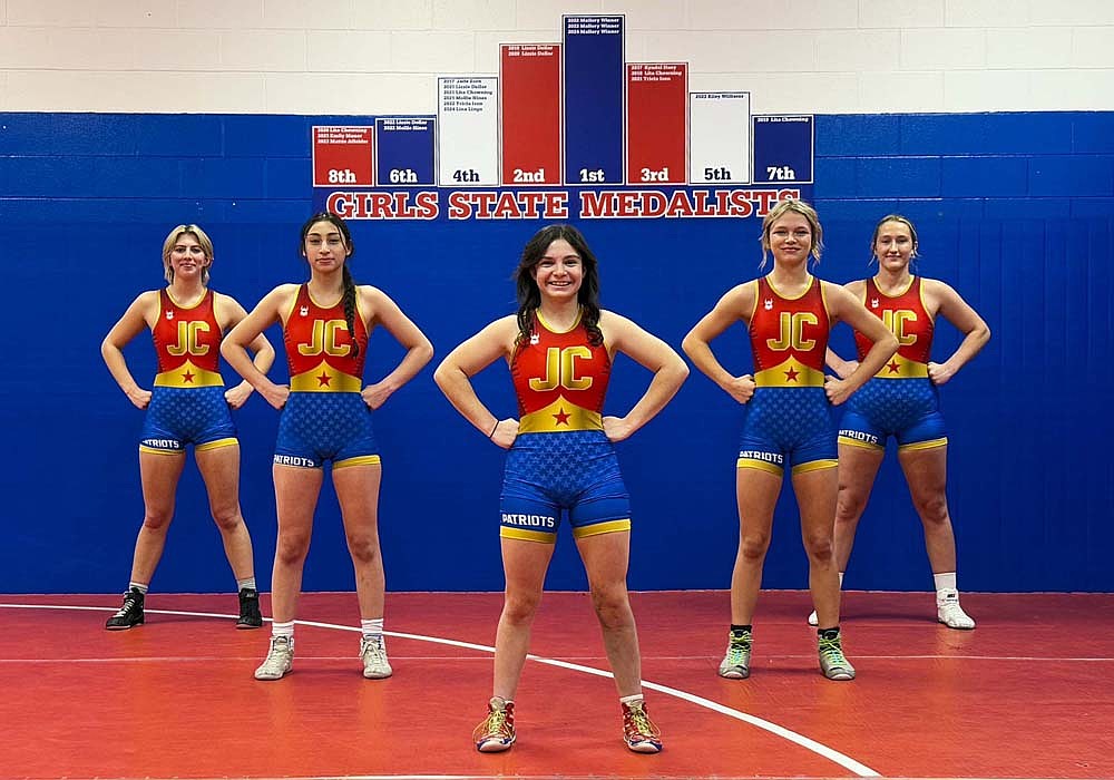 The five Jay County High School girls wrestlers pose with their new singlets designed by Katie Rowles (middle) inspired by both Wonder Woman and her first pair of wrestling shoes, which she is wearing in the photo. From left are Lina Lingo, Tatianna Willis, Rowles, Brenna Ruble and Mallory Winner. The Patriots will debut the singlets today at the inaugural IHSAA State Finals at Corteva Coliseum at Indiana State Fairgrounds. (The Commercial Review/Andrew Balko)