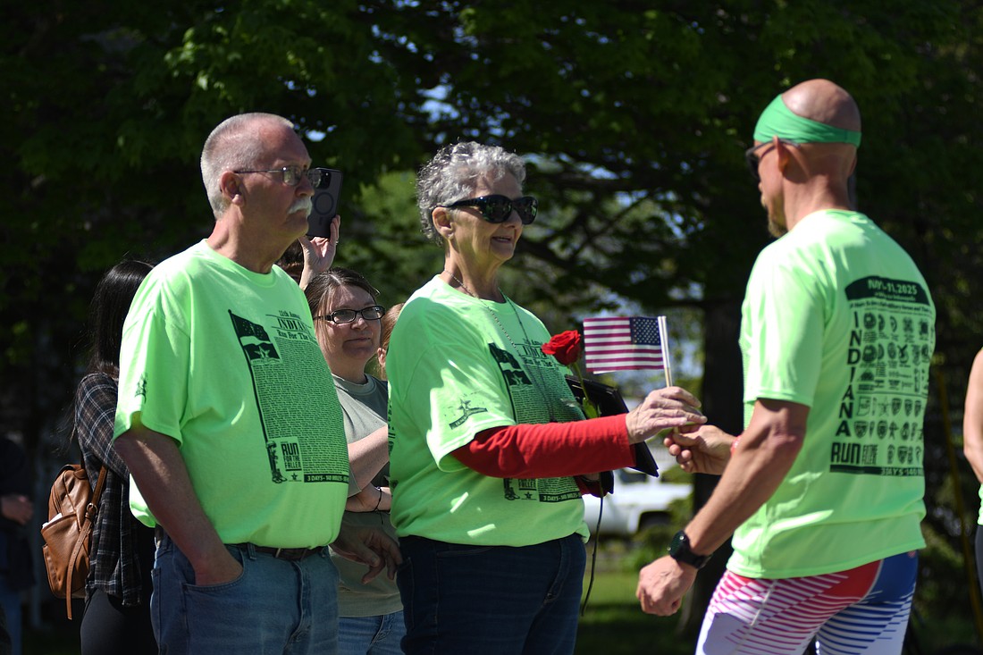 Runner Eric Butcher of Portland hands a flag to Norma Whitacre alongside her husband Ernie at the mile marker in Bryant honoring Marine Lance Cpl. Andrew F. Whitacre during Friday’s opening day of the Indiana Run for the Fallen. The first day started in Fort Wayne and concluded at Freedom Park in Portland, departing Saturday for a 58-mile second leg ending in Anderson. Runners will travel the final 30 miles to Indianapolis on Sunday. (The Commercial Review/Ray Cooney)