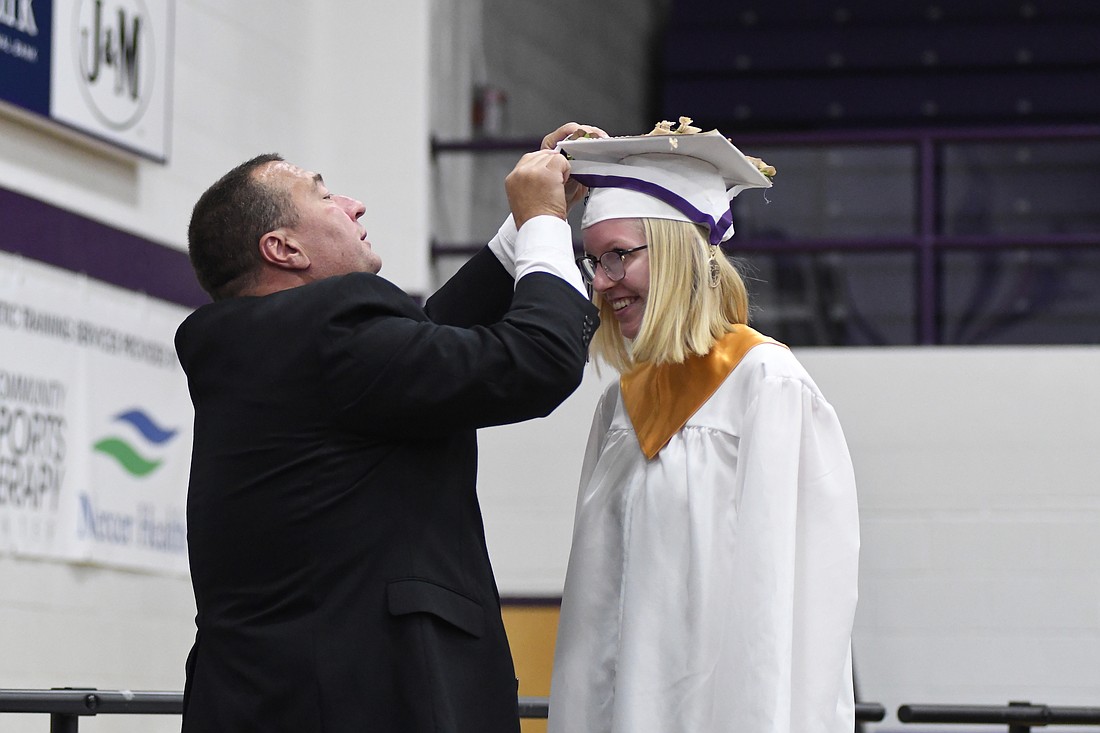 Fort Recovery High School senior Ava Englehardt grins Sunday while school board member Don Wendel struggles to get the activity key around her neck during the commencement ceremony at Fort Site Fieldhouse. Englehardt and Zach Schoenlein earned the activity key honors for their participation and leadership across a wide variety of extracurriculars. (The Commercial Review/Ray Cooney)