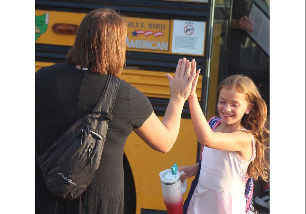 Fort Recovery Middle School principal Holly Wermert gives a high-five to fourth grader Mia Schoenlein as she gets off the bus Tuesday morning. Fort Recovery Local Schools students returned to the classroom Tuesday. (The Commercial Review/Bailey Cline)