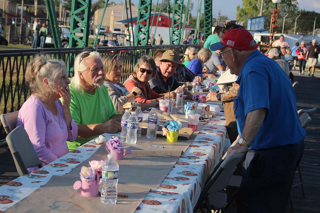 Local residents chat Thursday evening on the green bridge connecting Hudson Family Park and Weiler-Wilson Park in Portland. Jay County locals hosted a community dinner on the bridge, inviting residents to picnic or grab a meal from nearby food trucks and converse with others at tables set up along the bridge. (The Commercial Review/Bailey Cline)