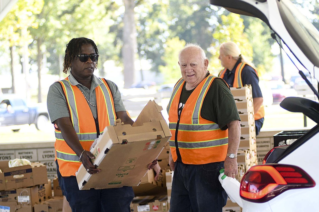 Dallas Sloss and Bill Sipe carry items to place in a vehicle during a food tailgate event Wednesday morning at Jay County Fairgrounds. Sloss, who works with Humana, and Sipe were volunteering for the monthly food giveaway sponsored by United Way of Jay County and Second Harvest Food Bank of East Central Indiana. (The Commercial Review/Ray Cooney)