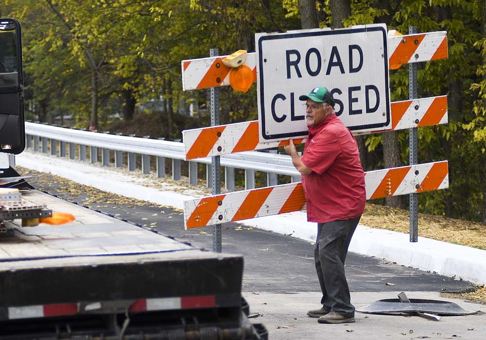 Tim Gillum from Brumbaugh Construction of Arcanum, Ohio, removes a road closed sign from the east side of the Seventh Street bridge over the Salamonie River in Portland on Wednesday afternoon. A project to rehabilitate the bridge and add a sidewalk on the north side is complete. (The Commercial Review/Ray Cooney)