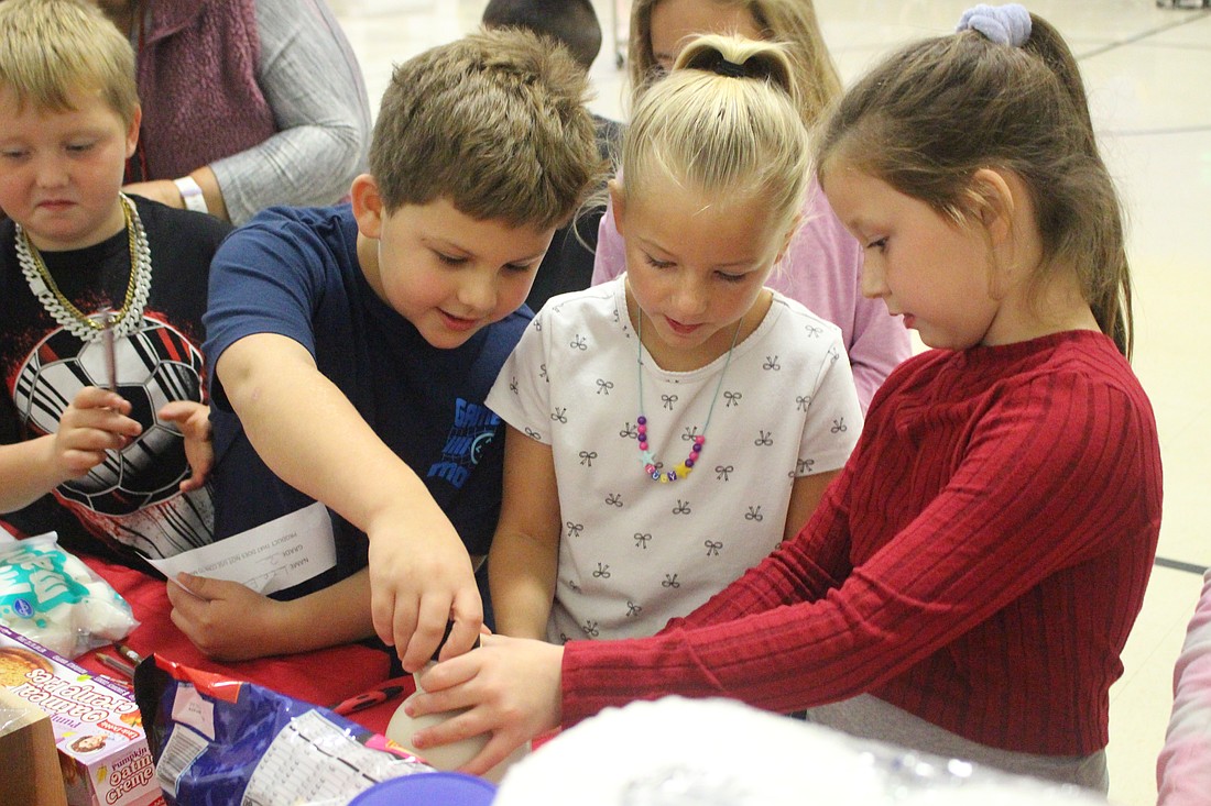 East Elementary School second graders Leo Esquivel, Lucy Loyd and Scarlett Cox look at a bottle of pure maple syrup Monday. Students were asked to guess which product presented on a table didn’t contain corn. (It was the maple syrup.) Jay County Farm Bureau and food service Chartwells recently partnered on a corn-focused program for Jay School Corporation, offering students the opportunity to learn more about corn. (The Commercial Review/Bailey Cline)