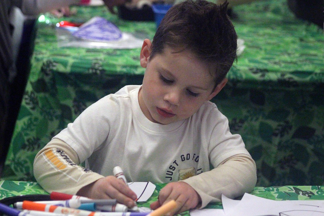 Jaxson Cook, 7, Portland, colors in a paper volcano Thursday during Jay County Public Library’s “Jump into Jurassic” interactive dinosaur experience. The library offered themed activities for children, including digging for fossils and exploring caves, prehistoric cave drawings and other crafts. (The Commercial Review/Bailey Cline)