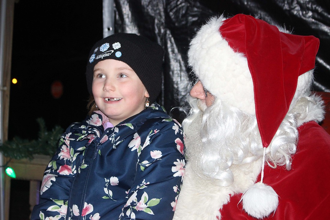 Santa Claus made his annual ride on a firetruck Friday into Redkey. Pictured at right, Kassidy Kirby, 7, tells Santa what she wants for Christmas at the downtown gazebo. Redkey Community Development Corporation also offered free hot chocolate, cookies, coloring pages and seating for families Friday evening at the old fire station. (The Commercial Review/Bailey Cline)