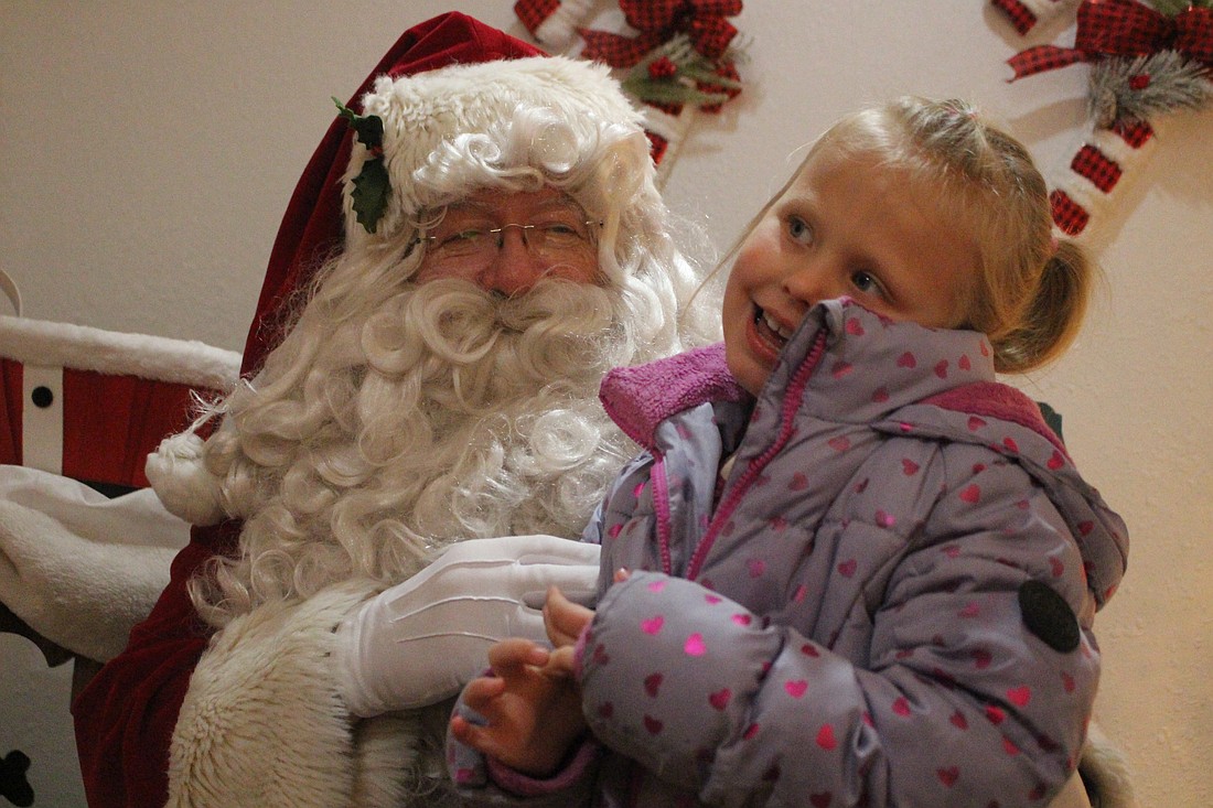 Luella Bales, 6, shares her Christmas wish list Friday with Santa at the Santa House on Main Street in Portland. Santa stopped by his spot in Portland for pictures with children, with families forming a line along the street. (The Commercial Review/Bailey Cline)