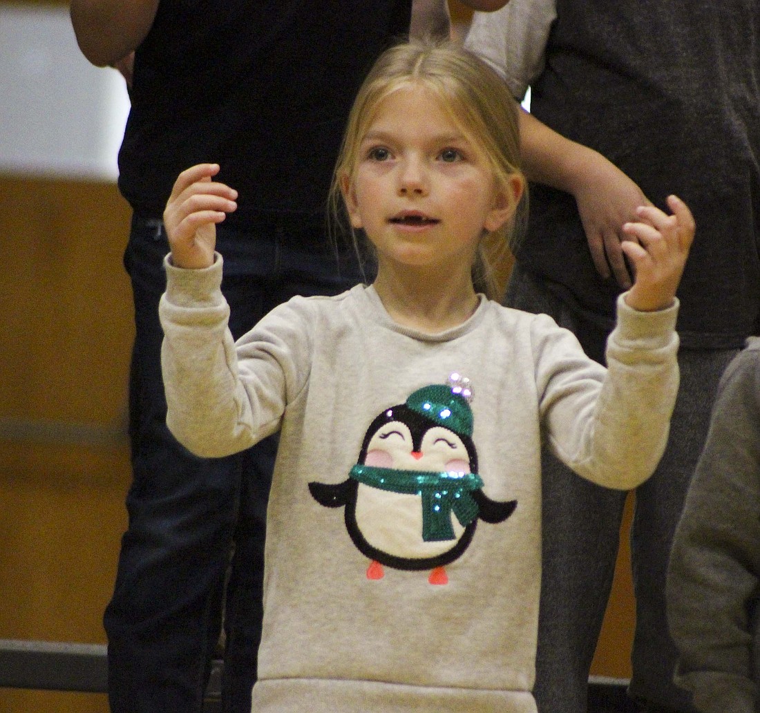 First grader Gracie Sanderson raises her hands while singing in Bloomfield Elementary School’s Christmas concert practice Thursday at East Jay Elementary School. (The Commercial Review/Bailey Cline)