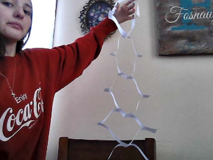 Allianna Fosnaugh, an eighth grader at Jay County Junior-Senior High School, shows off the result of her remote learning project for Meg Mauger’s engineering class this week. Students were tasked with cutting a hole in a single sheet of paper in such a way that they could fit their whole body through it. (Photo provided)